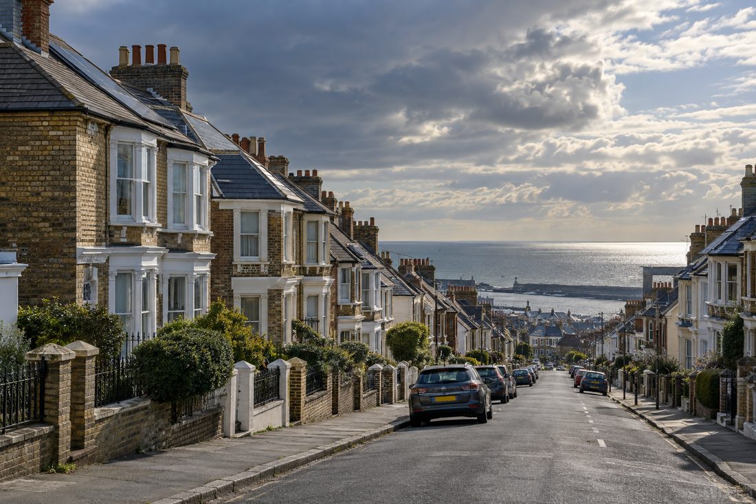 Street of Victorian brick terraced houses with bay windows and slate roofs, sloping down towards the sea at the end of the road